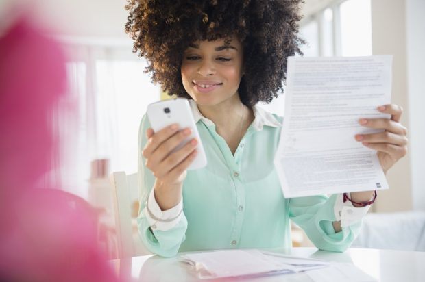 Woman looking at mobile phone and paper bill